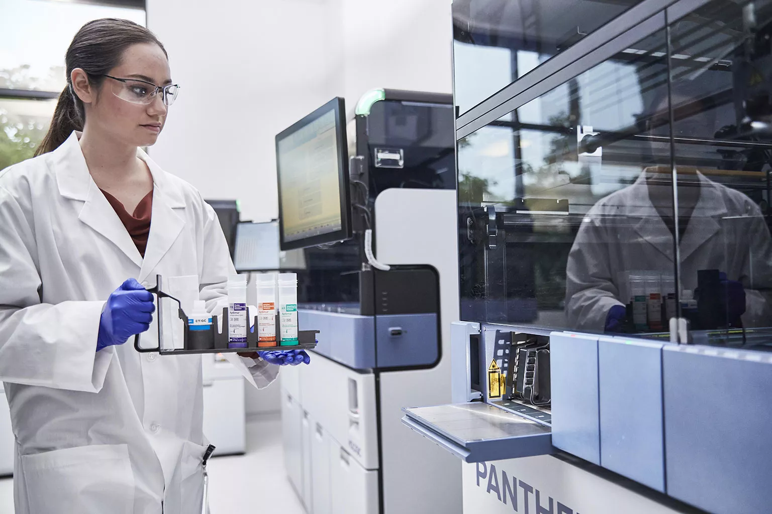 Ärztin beim Halten eines Probentrays neben dem Panther System in Laborumgebung.